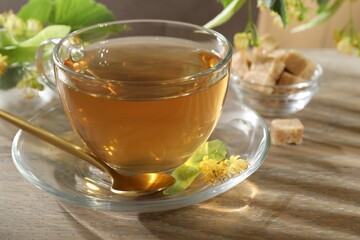 Tasty linden tea in cup, spoon, leaves and flowers on wooden table, closeup