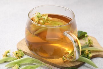 Fresh linden tea in cup and flowers on light grey table, closeup