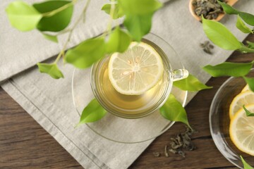 Refreshing green tea with lemon and leaves on wooden table, flat lay