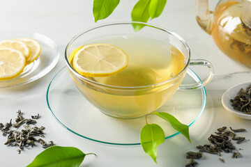Refreshing green tea with lemon and leaves on white marble table, closeup