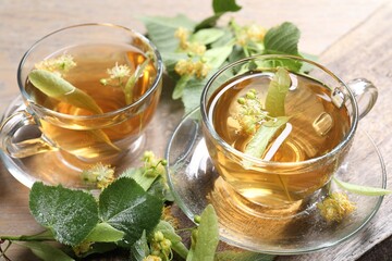 Tasty linden tea in cups, leaves and flowers on wooden table, closeup