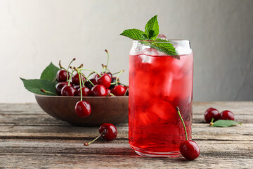 Tasty cherry soda with ice cubes, berries and mint on wooden table, closeup