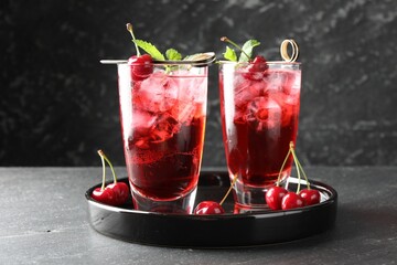 Tasty cherry soda with ice cubes, berries and mint in glasses on grey table, closeup