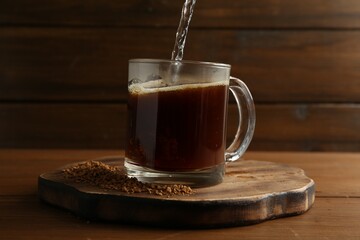 Pouring hot water into cup with instant coffee on wooden table, closeup