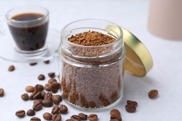 Instant coffee in glass jar, beans and hot drink on light grey table, closeup