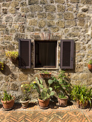 rustic stone wall with a small window with brown shutters and potted plants, set on a brick-paved ground. traditional