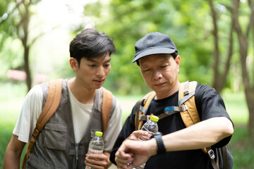 Father and Son Checking Time on Hike. A father and son pause to check their progress during an...