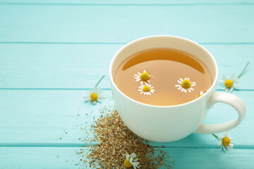 Aromatic herbal tea in white cup and chamomiles on blue wooden background. Space for text