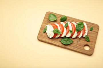Mozzarella cheese with green basil leaves and tomato on cutting board on beige background