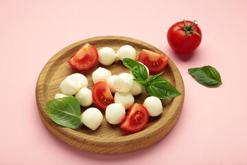 Italian Caprese salad with cherry tomatoes, mozzarella, basil on wooden plate on pink background.