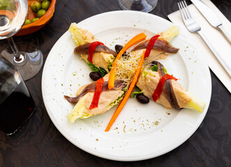 Delicious appetizer of fresh young hearts of Romaine lettuce topped with piquant sauce of goat cheese sauce with honey and walnuts served with anchovy fillets, backed bell pepper and black olives