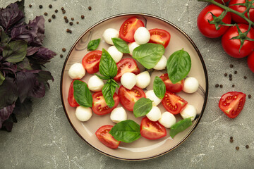 Italian Caprese salad with cherry tomatoes, mozzarella, basil on plate on grey concrete background.