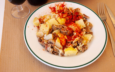 Galician dish of stewed pig's ear with red pepper and potatoes at plate on table