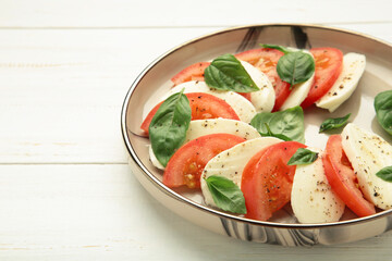 Italian Caprese salad with cherry tomatoes, mozzarella, basil on plate on white background.