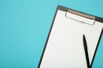 Pen and black clipboard with paper on blue background.