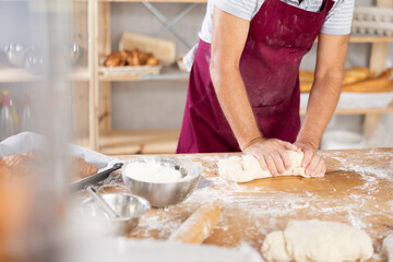 Elderly baker hands kneading dough on table, close-up