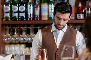 Close-up portrait of a handsome, attentive young bartender with a beard, wearing a vest and listening to an order at a classic bar. Professional service in a restaurant.