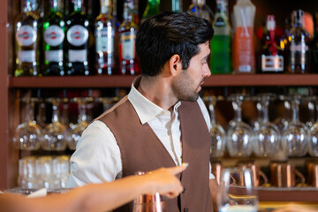 Close-up portrait of a handsome, attentive young bartender with a beard, wearing a vest and listening to an order at a classic bar. Professional service in a restaurant.