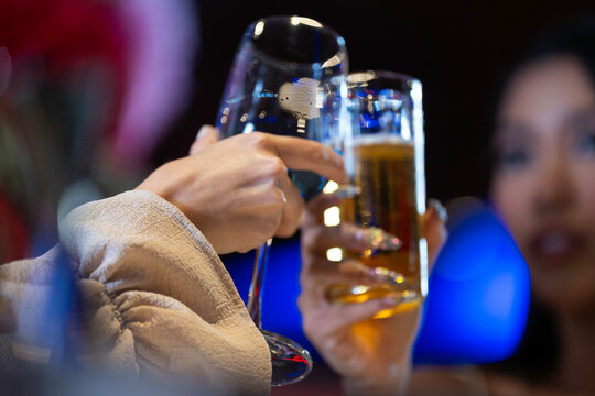 Close-up of two female friends toasting and clinking glasses of wine and beer in a bar at night. Concept of celebration, friendship, success, and happy hour. - Powered by Adobe