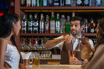 Expatriate bartender skillfully preparing cocktails for two beautiful female customers at a stylish...