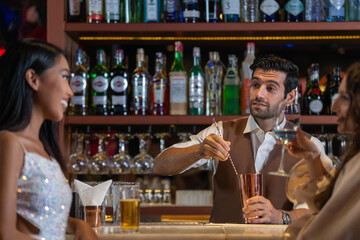 Expatriate bartender skillfully preparing cocktails for two beautiful female customers at a stylish bar counter in Bangkok, Thailand. Warm atmosphere and friendly service in a vibrant city.