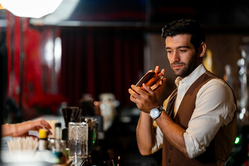 A handsome and focused professional bartender concentrating as he prepares a craft cocktail with a copper shaker in a stylish, dark bar at night.
