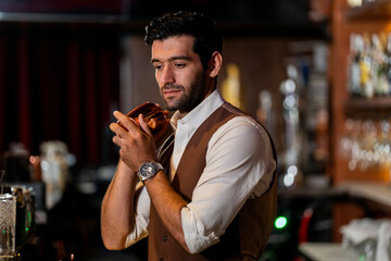 A handsome and focused professional bartender concentrating as he prepares a craft cocktail with a copper shaker in a stylish, dark bar at night.