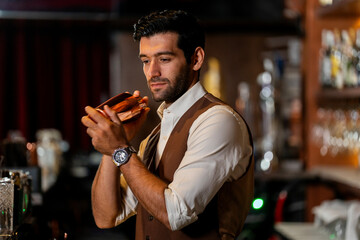 A handsome and focused professional bartender concentrating as he prepares a craft cocktail with a copper shaker in a stylish, dark bar at night.