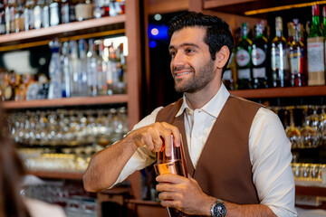 A handsome and focused professional bartender concentrating as he prepares a craft cocktail with a copper shaker in a stylish, dark bar at night.