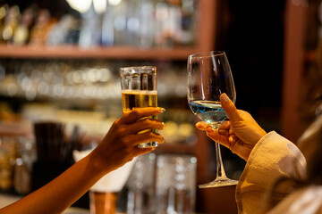 Two female friends raising glasses of beer and a blue cocktail for a toast in a stylish bar. Concept of celebration, friendship, and happy hour on a night out in Bangkok.