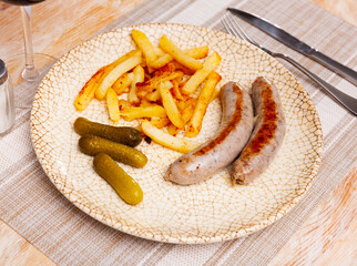 Tasty hearty lunch of roasted meat sausages with french fried potatoes and pickled cucumbers
