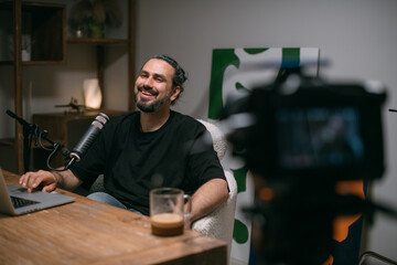 Video podcast recording studio. A young man is sitting at a table in front of a microphone in the...