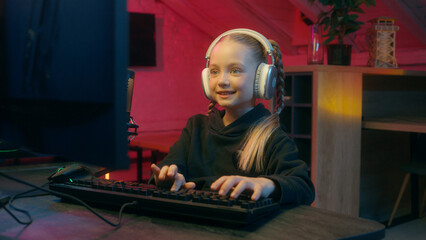 Happy smiling little Caucasian girl child kid daughter gamer in wireless headphones modern...