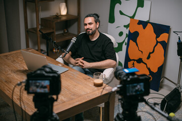 Video podcast recording studio. A young man is sitting at a table in front of a microphone in the...