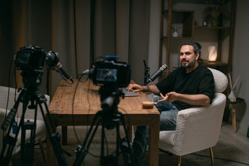 Video podcast recording studio. A young man is sitting at a table in front of a microphone in the...