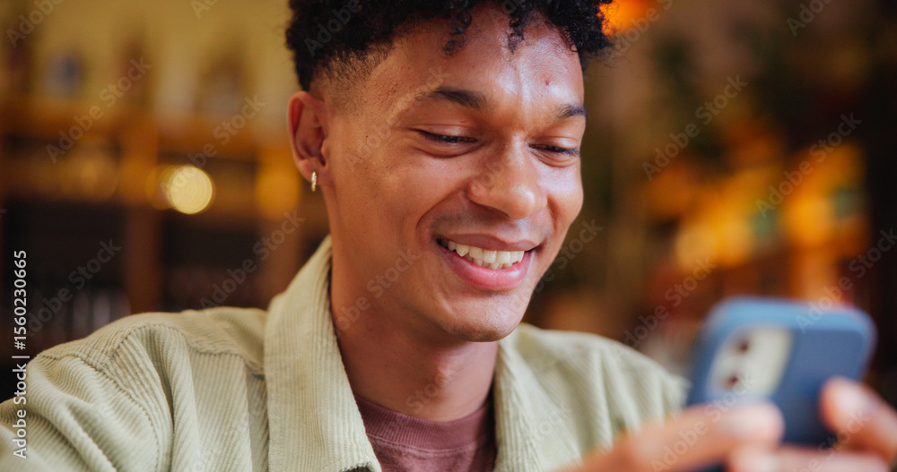 Poster man, smartphone and texting with smile at cafe with contact, typing and streaming on web at restaura
