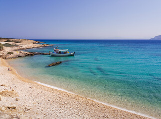 Scenic Greek island beach with turquoise waters and a small fishing boat anchored near the shore. Koufonisia Islands, Cyclades, Greece