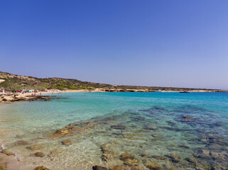 Crystal clear turquoise waters of a Mediterranean beach with rocky coastline and distant hills. Koufonisia Islands, Cyclades, Greece