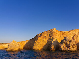 Stunning coastal landscape with golden rocky cliffs against clear blue sky and calm sea waters. Koufonisia Islands, Cyclades, Greece