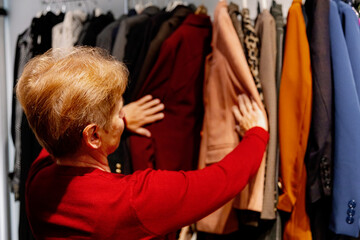 Senior women in red blouses choose a new jacket in a boutique.