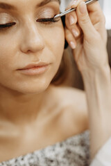 Eyelash extensions. Makeup artist applies eyelashes to model eyes. Vertical view