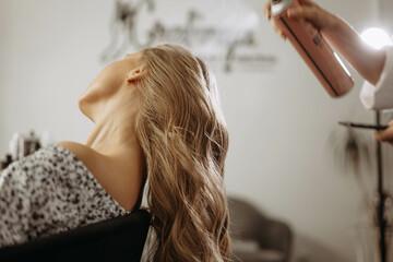 Makeup artist hairdresser sprays hairspray on model head and hair