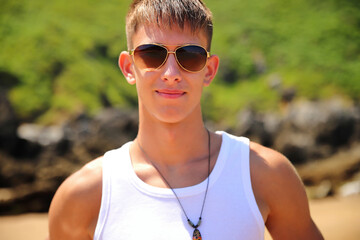 Young guy in sunglasses on the beach, casual teenager style, summer lifestyle