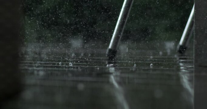 Close up of rain drops bouncing off wet wood near metal chair leg, recorded in super slow motion with high speed camera, garden scene in background