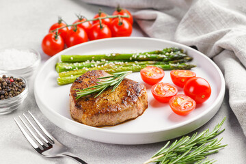 Close up, macro of tasty grilled beef steak served with green asparagus and cherry tomatoes on white plate, with cutlery. Perfect for food menu, diet, or culinary design concepts.