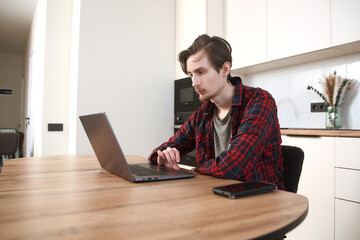 a young man  concentrate our energy and using a laptop, connecting to the Internet in the kitchen...