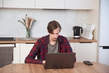 a young man  concentrate our energy and using a laptop, connecting to the Internet in the kitchen...