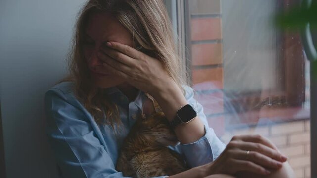 Unhappy beauty woman crying sitting on windowsill, window rain drops dark rainy weather, mood depression sadness loneliness emotion at home room. Adult upset Girl sad face tears pain grief. holds cat