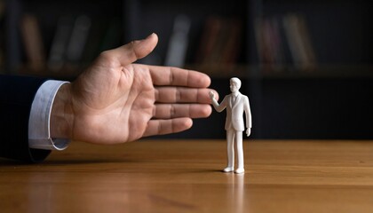 A tiny figurine representing a person stands near a giant hand, symbolizing control, power or vulnerability. The contrast between the hand and the figurine creates a compelling visual