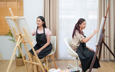 Two young asian woman artist painting on canvas. Female artist drawing with inspiration at home